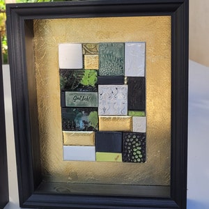 Könnte beinhalten: Ein gerahmtes Mosaik-Kunstwerk mit goldenem Hintergrund und schwarzem Rahmen. Das Mosaik besteht aus kleinen, quadratischen Fliesen in verschiedenen Grüntönen, Schwarz und Weiß. Der Text "Good Luck!" ist in der Mitte des Kunstwerks sichtbar.