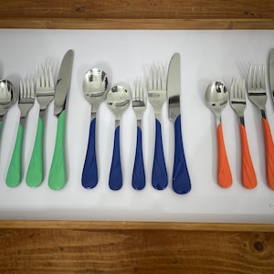 May include: A set of stainless steel flatware with colored handles. The set includes spoons, forks, and knives with green, blue, and orange handles. The flatware is arranged on a white surface inside a wooden tray.