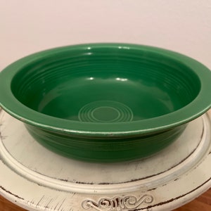 May include: A green ceramic bowl with a wide rim and a smooth, glossy finish. The bowl has a simple, classic design and is perfect for serving salads, snacks, or desserts.