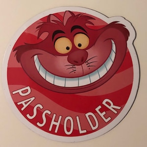 May include: A red and white round magnet with a cartoon image of the Cheshire Cat from Alice in Wonderland. The text "PASSHOLDER" is written in white letters around the bottom of the magnet.