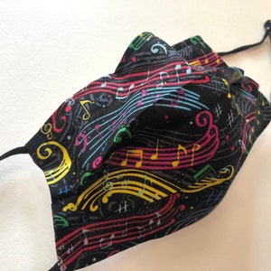 May include: Black face mask with a colorful musical notes pattern. The notes are in various colors, including red, yellow, blue, and green. The mask has elastic ear loops.
