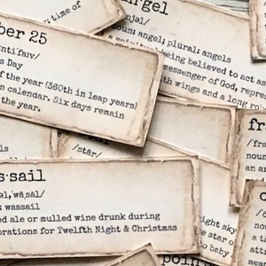 May include: Close-up of several vintage-style cards with definitions of words like "December 25", "was-sail", "angel", "frank-incense", and "ornament". The cards are printed on cream-coloured paper with brown edges and have a distressed, aged look.