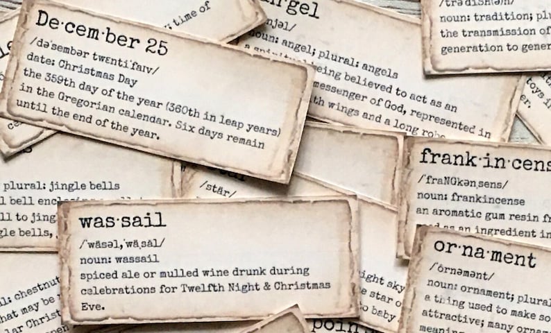 May include: Close-up of several vintage-style cards with definitions of words like "December 25", "was-sail", "angel", "frank-incense", and "ornament". The cards are printed on cream-coloured paper with brown edges and have a distressed, aged look.
