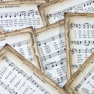 Pu&ograve; includere: Una collezione di spartiti musicali vintage con canti natalizi, tra cui "Tu scendi dalle stelle", "Adeste Fideles", "Astro del ciel", e "Oh, Holy Night". La musica &egrave; stampata su carta invecchiata con un aspetto usurato e sbiadito.