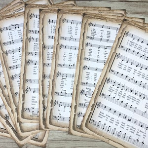 Pu&ograve; includere: Una collezione di pagine di spartiti musicali vintage con un aspetto usurato e invecchiato. Le pagine presentano notazione musicale e testi per vari inni e canti natalizi, tra cui "Hark! The Herald Angels Sing".