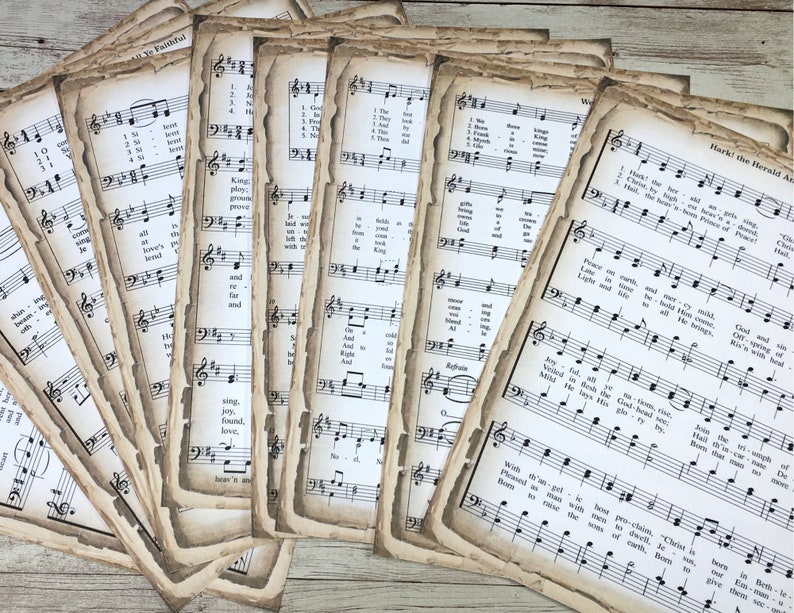 Pu&ograve; includere: Una collezione di pagine di spartiti musicali vintage con un aspetto usurato e invecchiato. Le pagine presentano notazione musicale e testi per vari inni e canti natalizi, tra cui "Hark! The Herald Angels Sing".