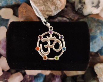 May include: Silver Om pendant with seven colorful gemstones arranged in a circle. The gemstones are red, orange, yellow, green, blue, indigo, and violet.