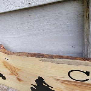 May include: A wooden sign with a natural edge, featuring a silhouette of a person riding a motorcycle. The sign has the text "Live Co" in black lettering.