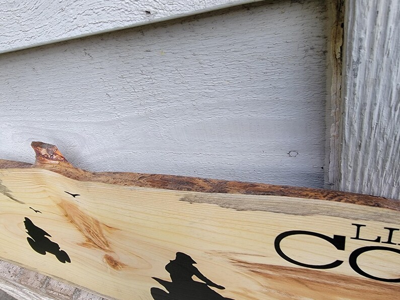 May include: A wooden sign with a natural edge, featuring a silhouette of a person riding a motorcycle. The sign has the text "Live Co" in black lettering.