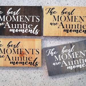 Könnte beinhalten: Vier Holzschildchen mit dem Text "The best MOMENTS are Auntie moments" in schwarz-weißer Schrift. Die Schilder sind aus verschiedenen Holzarten gefertigt, zwei Schilder haben eine helle Holzoptik und zwei Schilder eine dunkle Holzoptik.