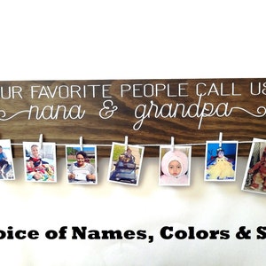 May include: A brown wooden sign with the text "OUR FAVORITE PEOPLE CALL US nana & grandpa" in white lettering. The sign has a string of clothespins attached to it, and there are photos of children clipped to the clothespins.