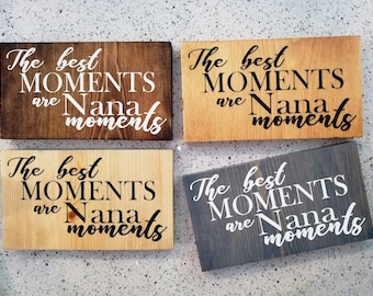 May include: Four wooden signs with the text "The best moments are Nana moments" in black and white lettering. The signs are on a white surface.