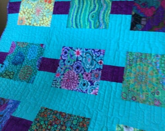 May include: A turquoise quilt with purple squares and a variety of colorful floral and geometric patterns.