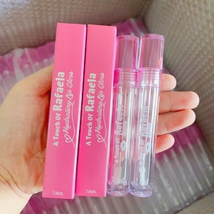 May include: Two pink and white boxes with the text "A Touch of Rafaela Hydrating Lip Gloss" and "7.8ML" printed on them. Two clear lip gloss tubes with pink caps and the text "A Touch of Rafaela Beauty" printed on them.