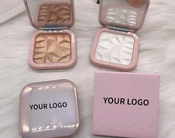 May include: Two square compact makeup palettes with a pink and white design. The palettes have a mirror on the top and a pressed powder inside. The powder is a light gold color in one palette and a white color in the other. The palettes are sitting on a white surface with a pink box that says "YOUR LOGO" on it.
