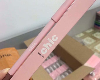 May include: A pink lip liner pencil with the word "chic" written on it in white letters. The pencil is in a pink box with the words "chic cosmetics" and "long lasting lip liner" printed on it.