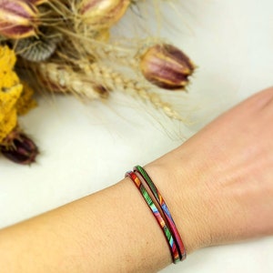 May include: A colorful patterned bracelet wrapped twice around a wrist. The bracelet is made of thin leather and has a red, green, blue, and yellow pattern.