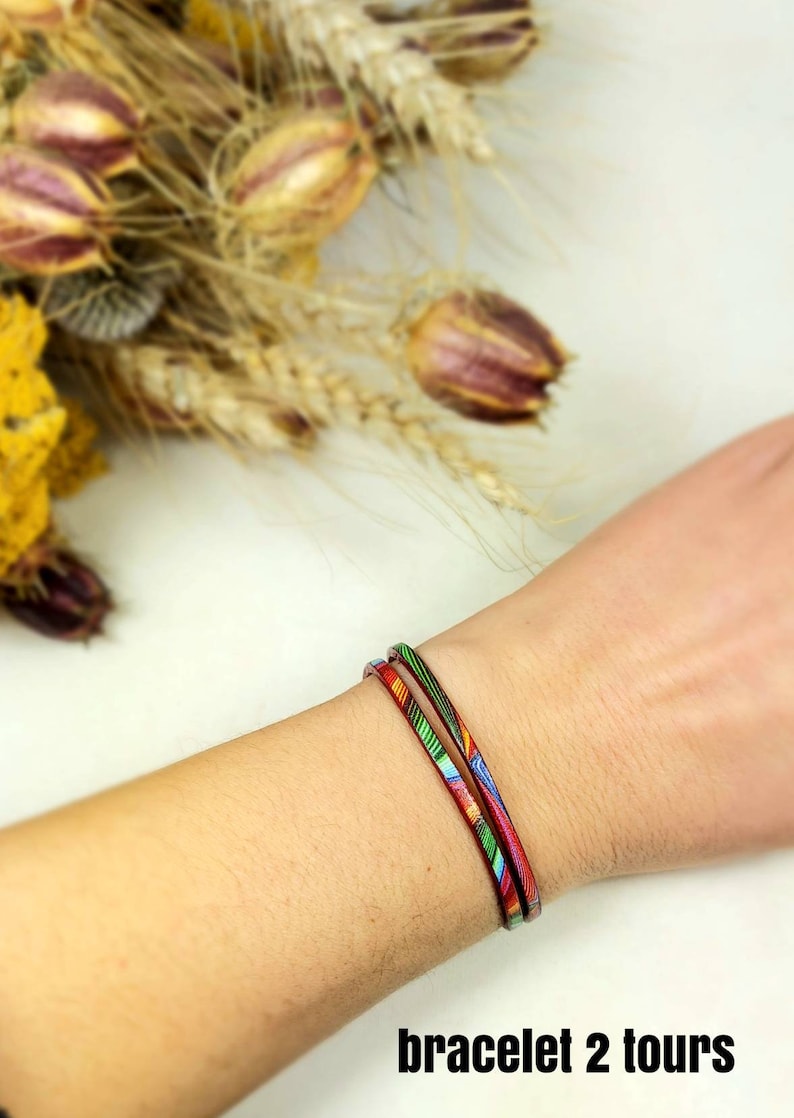 May include: A colorful patterned bracelet wrapped twice around a wrist. The bracelet is made of thin leather and has a red, green, blue, and yellow pattern.