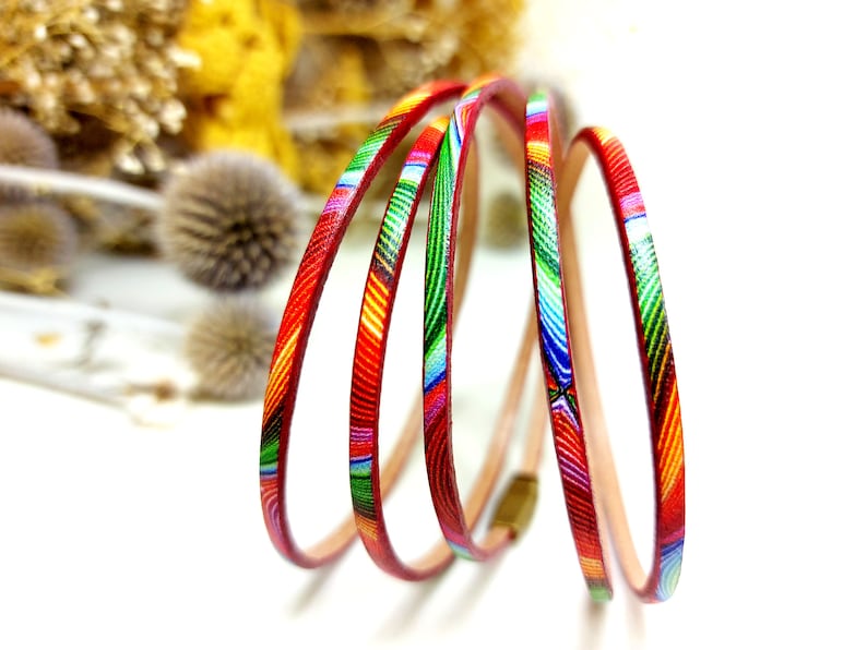 May include: Multicolored leather cord with a geometric pattern in shades of red, green, blue, and yellow. The cord is coiled and ready to be used for jewelry making or other crafts.
