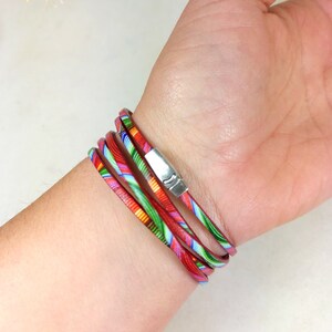 May include: Multi-colored leather wrap bracelet with a silver clasp. The bracelet is made of several thin strips of leather that are woven together. The leather is printed with a colorful pattern.
