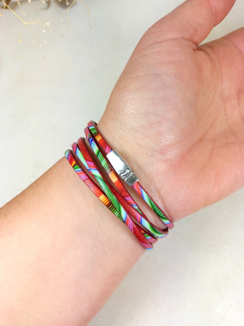 May include: Multi-colored leather wrap bracelet with a silver clasp. The bracelet is made of several thin strips of leather that are woven together. The leather is printed with a colorful pattern.