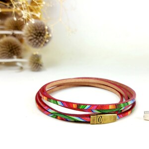 May include: A red leather bracelet with a colorful geometric pattern. The bracelet is made of three strands of leather and has a silver clasp.
