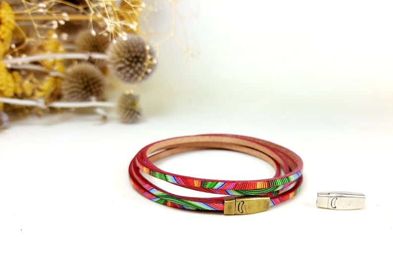 May include: A red leather bracelet with a colorful geometric pattern. The bracelet is made of three strands of leather and has a silver clasp.
