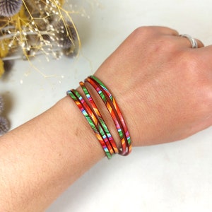 May include: A set of five colorful bangles with red, orange, yellow, green, and blue stripes. The bangles are stacked on a person's wrist.