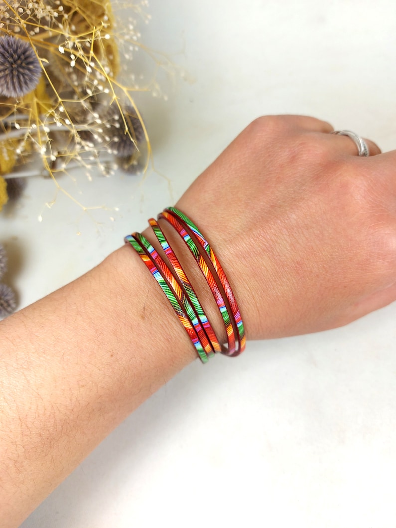 May include: A set of five colorful bangles with red, orange, yellow, green, and blue stripes. The bangles are stacked on a person's wrist.