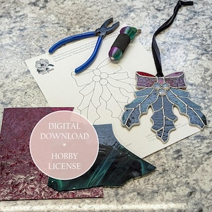 May include: A stained glass holly leaf ornament with a red and purple bow, blue leaves, and clear gems. Also shown are glass pieces, a pattern, and tools. The image includes the text "DIGITAL DOWNLOAD * HOBBY LICENSE".