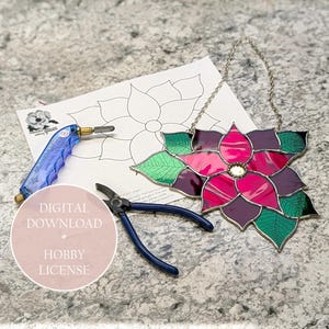 以下が含まれることがあります： グレーのカウンタートップに、銀色のチェーン、ガラスカッター、ペンチが付いたステンドグラスのポインセチアの花。画像には、デジタルダウンロードの趣味ライセンスも含まれています。