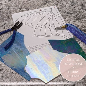 May include: A craft project setup featuring a printed pattern, glass pieces, and tools. The tools include blue-handled pliers and a glass cutter. The glass pieces have iridescent and blue hues. The image also includes the text "DIGITAL DOWNLOAD + HOBBY LICENSE."