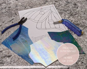 May include: A craft project setup featuring a printed pattern, glass pieces, and tools. The tools include blue-handled pliers and a glass cutter. The glass pieces have iridescent and blue hues. The image also includes the text "DIGITAL DOWNLOAD + HOBBY LICENSE."