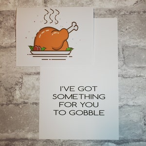May include: A white card with a cartoon illustration of a roasted turkey on a plate with green leaves and red berries. The card has the text "I've got something for you to gobble" in black.