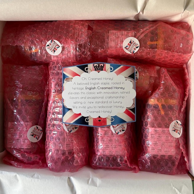 Open gift box showing six jars of English Creamed Honey carefully packaged in pink bubble wrap with “English Creamed Honey” stickers and a printed insert card describing the brand’s heritage. The presentation highlights the attention to detail and care taken to ensure each jar arrives safely and beautifully packaged