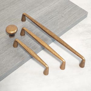 May include: A collection of antique bronze cabinet hardware, including a round knob and three different-sized pull handles. The hardware has a textured finish and a warm, aged appearance. The pulls are straight with curved ends.