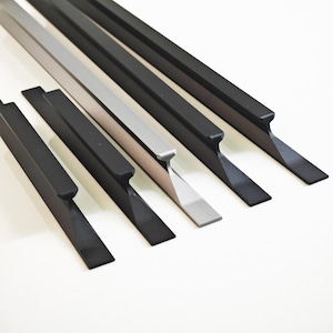 Op de afbeelding: Een assortiment metalen beitels in verschillende kleuren, waaronder zwart en zilver. De beitels hebben een plat, schuin blad en een rechthoekige handgreep. De gereedschappen zijn diagonaal geplaatst tegen een witte achtergrond.