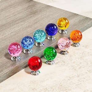 May include: A collection of ten colorful glass cabinet knobs. Each knob features a clear, spherical design with internal decorative elements and a silver-toned base. Colors include red, pink, blue, green, yellow, and orange. These knobs are suitable for furniture upgrades.