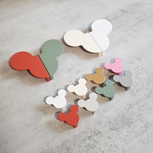 May include: A collection of colorful, Mickey Mouse-shaped cabinet knobs in various shades, including red, white, green, and pink. The knobs are made of wood and are arranged on a gray surface. The knobs are a fun and playful addition to any room.