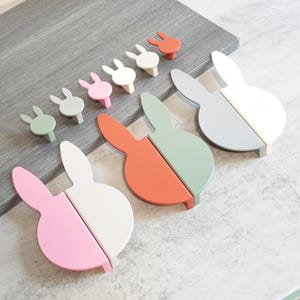 May include: A collection of colorful bunny-shaped cabinet knobs and pulls. The knobs are in shades of green, pink, white, and orange. The pulls are split into two halves, with each half in a different color. These decorative knobs and pulls are perfect for a child's room or nursery.