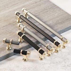 May include: A selection of cabinet handles and knobs. The handles have a gold-coloured base with black and silver ribbed bars. The knobs have a gold-coloured base with black and silver ribbed bars. The hardware is designed for cabinets and drawers, with a range of sizes.