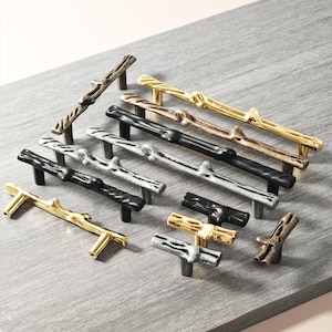 May include: A selection of cabinet handles and knobs in gold, silver, bronze, and black. The hardware is designed to look like twigs and branches, offering a natural, rustic style. The handles and knobs are suitable for various furniture.