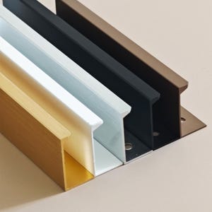 May include: A close-up of a selection of metal drawer pulls in various colors. The pulls are in gold, white, black, and bronze. Each pull has a unique shape and is mounted on a metal plate.