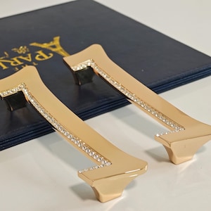 Peut inclure: Deux poignées de placard dorées en forme de chiffre sept, bordées de strass en cristal. Le fond est une surface bleu foncé avec du texte doré et un motif de la Tour Eiffel dorée.