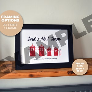 Pu&ograve; includere: Una stampa incorniciata con il testo "Dad's No.1 Team" e una grafica di quattro maglie rosse con numeri su di esse. Le maglie hanno i nomi "Daddy", "Mummy", "02" e "04" su di esse. La cornice &egrave; nera e la stampa &egrave; su carta bianca. La dimensione della cornice &egrave; di 35 cm x 26 cm.