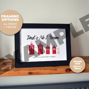 May include: A framed print with the text "Dad's No.1 Team" and a graphic of four red jerseys with numbers on them. The jerseys have the names "Daddy", "Mummy", "02", and "04" on them. The frame is black and the print is on white paper. The frame size is 35cm x 26cm.