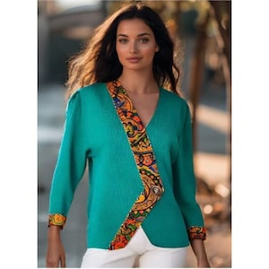 May include: Teal V-neck sweater with long sleeves. The sweater features a colorful patterned design along the front and cuffs. A decorative button accents the wrap-style closure. The model is wearing white pants.