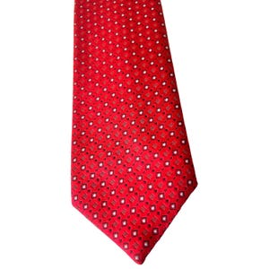 May include: A red necktie with a repeating pattern of small white and brown squares. The tie is made of a smooth fabric and is suitable for formal or business attire.