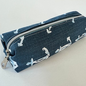 May include: A dark blue pencil case with a zipper closure and a white anchor pattern. The case has a silver zipper pull with a loop.