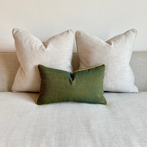 May include: Two light beige throw pillows with a dark green throw pillow in the centre. The pillows are on a light beige sofa.
